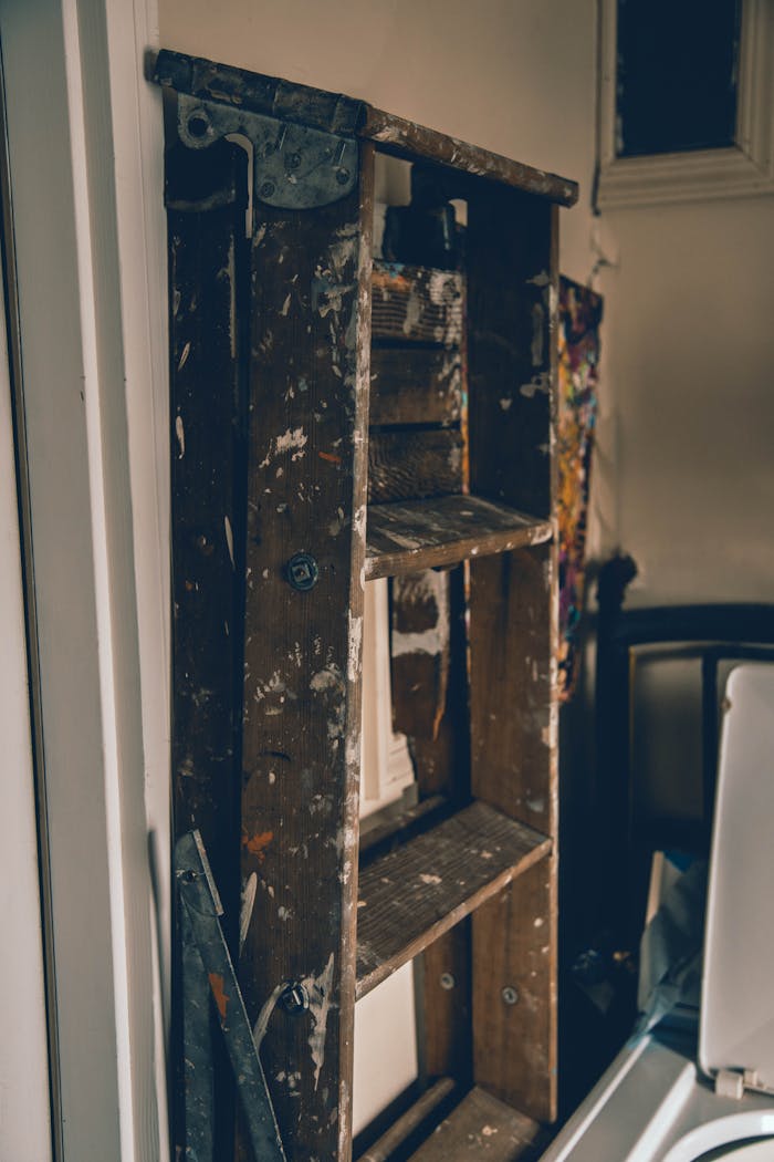 A worn wooden ladder with paint splatters resting in a cozy indoor environment.