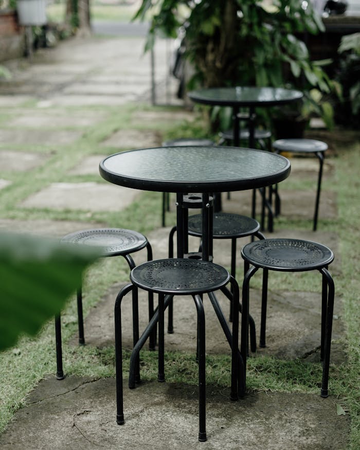 Black metal stools and round glass table set on a lush green outdoor patio.