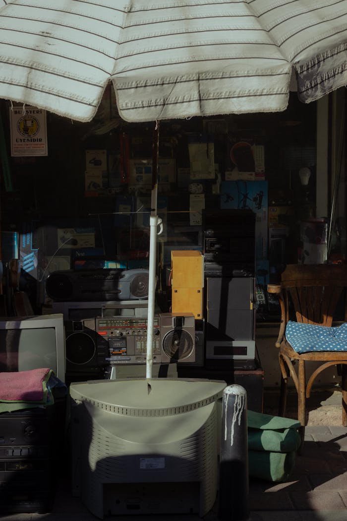 Outdoor display of vintage electronics, furniture, and a parasol at an antique shop.