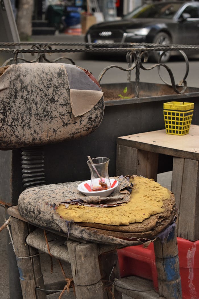 A weathered chair with an empty tea glass sits abandoned on a city street.