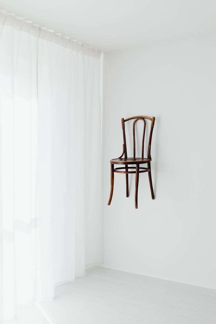 Elegant minimalist room featuring a wooden chair attached to a white wall.